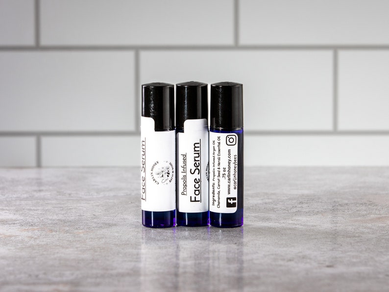 May include: Three small blue glass bottles with black roll-on tops. The bottles are labeled "Face Serum" and "Propolis Infused Face Serum". The labels also include the brand name "Carlin Honey" and the website address "www.carlinhoney.com".
