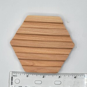 May include: A hexagonal wooden soap dish with grooves on the surface. The dish is approximately 3 inches wide.