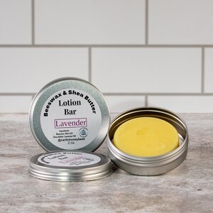 May include: A silver tin with a label that reads "Beeswax & Shea Butter Lotion Bar Lavender" and contains a yellow lotion bar. The tin is 2 oz.
