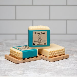 May include: Three bars of honey soap with a blue and white label that reads "Honey Soap" and "Lavender Spearmint". The soap bars are on wooden soap dishes.