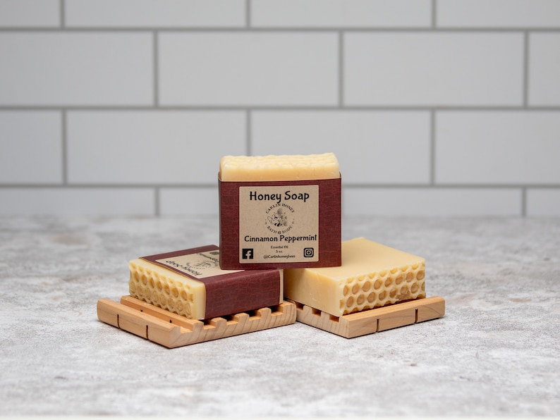 May include: Three bars of honey soap with a honeycomb design. The top bar has a brown label that reads "Honey Soap" and "Cinnamon Peppermint".