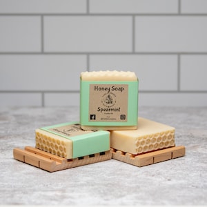 May include: Three bars of honey soap with a honeycomb design. The top bar has a brown label that reads "Honey Soap" and "Spearmint".