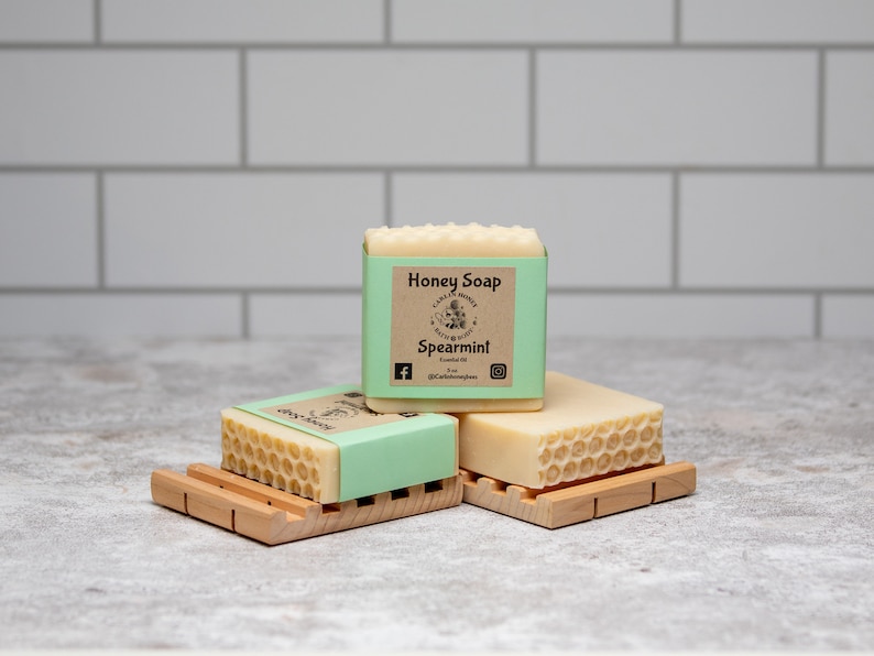 May include: Three bars of honey soap with a honeycomb design. The top bar has a brown label that reads "Honey Soap" and "Spearmint".