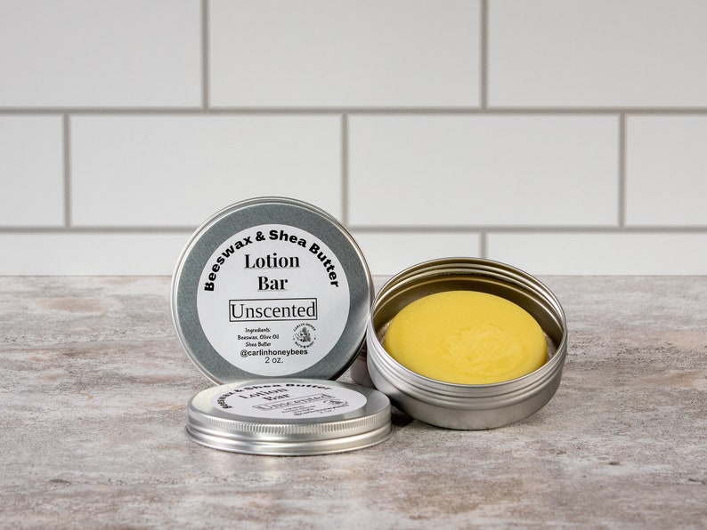 May include: A silver tin with a label that reads "Beeswax & Shea Butter Lotion Bar Unscented" and contains a yellow lotion bar. The tin is 2 oz.