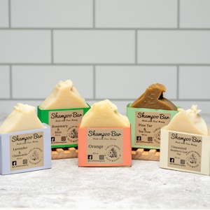 May include: Five rectangular shampoo bars with labels reading Shampoo Bar Made with Pure Honey. Scents include Lavender & Chamomile, Rosemary & Mint, Orange, Pine Tar & Tea Tree, and Unscented Raspberry Leaf Tea. Each bar weighs 4.5 oz.