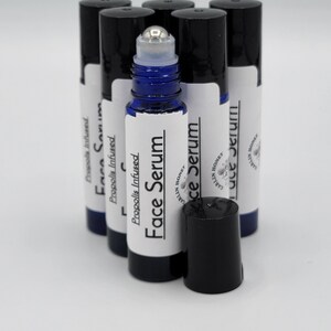 May include: A group of six blue glass roller bottles with black caps. The bottles are labeled "Propolis Infused Face Serum" and "Carlin Honey".