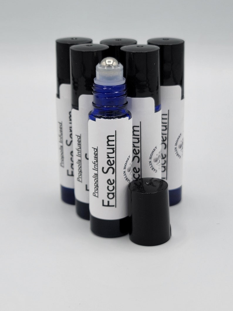 May include: A group of six blue glass roller bottles with black caps. The bottles are labeled "Propolis Infused Face Serum" and "Carlin Honey".