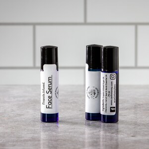 May include: Three small blue glass bottles with black roll-on tops and white labels. The labels have black text that reads "Propolis Infused Face Serum" and "Ingredients: Propolis Infused Argan Oil, Chamomile, Carrot Seed & Neroli Essential Oil. 0.75 oz. www.carlinhoney.com #acarlinhoneybees".