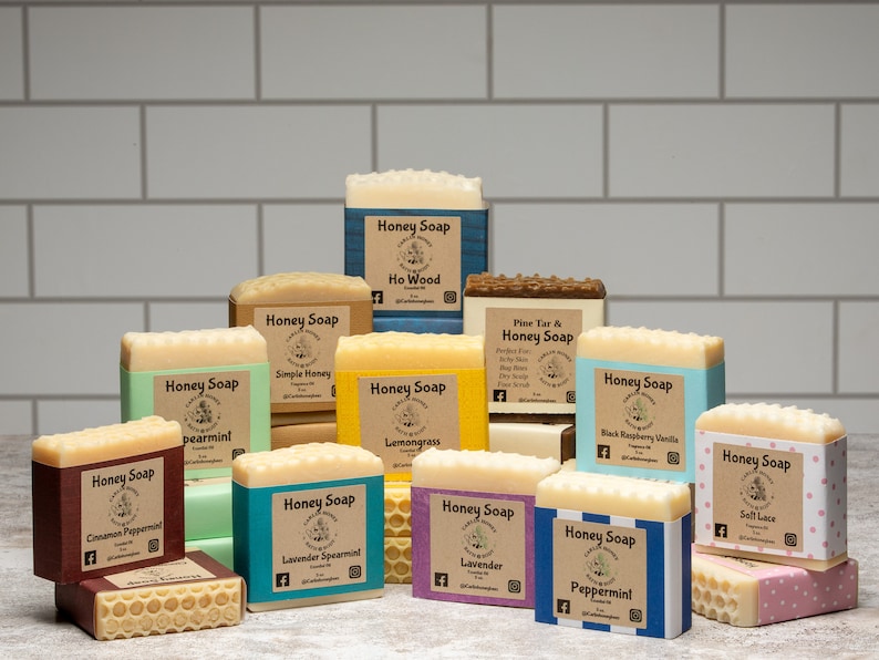 May include: Assortment of honey soap bars with various scents, including Ho Wood, Simple Honey, Pearmint, Lemongrass, Black Raspberry Vanilla, Cinnamon Peppermint, Lavender Spearmint, Lavender, Soft Lace, and Peppermint. Each bar is wrapped in colorful paper with a label that includes the scent and the brand name.