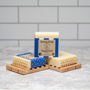 May include: Three bars of honey soap with a honeycomb pattern on the top. The bar in the middle has a blue and white label that says "Honey Soap" and "Peppermint".