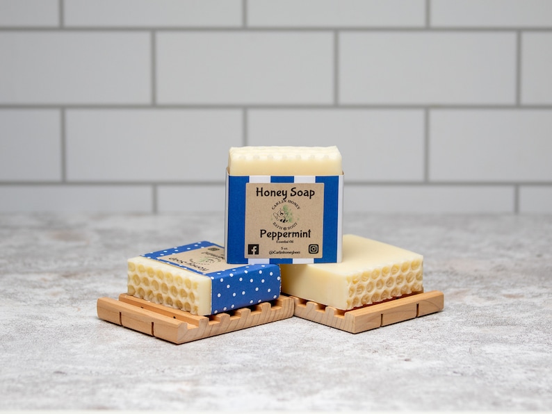 May include: Three bars of honey soap with a honeycomb pattern on the top. The bar in the middle has a blue and white label that says "Honey Soap" and "Peppermint".