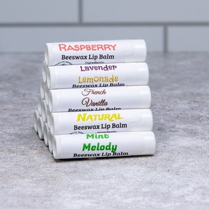 May include: A stack of ten white lip balm tubes with different flavor labels. The labels are in various colors and include Raspberry, Lavender, Lemonade, French Vanilla, Natural, Mint, and Melody.