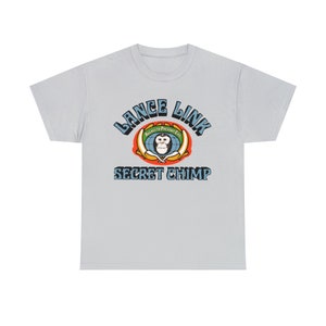 Puede incluir: Camiseta azul claro con un diseño gráfico retro. El diseño incluye el texto "LANCE LINK" en azul, arqueado sobre una imagen de un mono en un globo, y las palabras "SECRET CHIMP" debajo. La camiseta es de cuello redondo clásico.