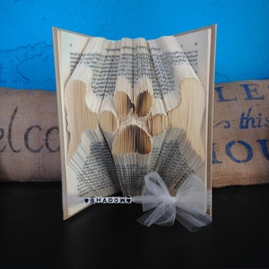 May include: A book folded into the shape of a paw print with a white tulle bow and a black beaded tag that says "SHADOW" on it.