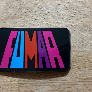 Könnte beinhalten: Ein schwarzer rechteckiger Aufkleber mit dem Wort "FUMAR" in bunten Buchstaben. Die Buchstaben sind in einer fetten, stilisierten Schriftart. Das "F" ist pink, das "U" ist blau, das "M" ist orange, das "A" ist lila und das "R" ist pink.