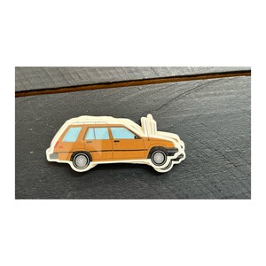 May include: A brown station wagon sticker with a white background. The car has a white roof rack and a blue windshield.