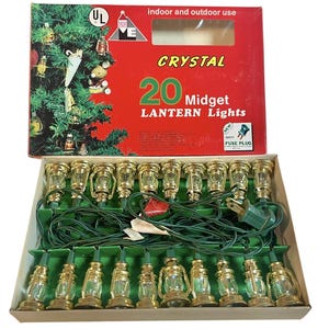 May include: A box of 20 Crystal Midget Lantern Lights. The lights are shaped like small lanterns with gold-colored frames and clear glass. The box is red with the text "Crystal 20 Midget Lantern Lights". The lights are for indoor and outdoor use.