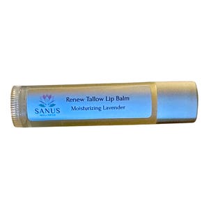 Op de afbeelding: Een cilindervormige lippenbalsemhuls met een lichtgekleurde dop en onderkant. Het etiket bevat een lotusbloem-icoon, de tekst SANUS WELLNESS en de woorden Renew Tallow Lip Balm Moisturizing Lavender in donkerblauw op een lichtblauwe achtergrond.
