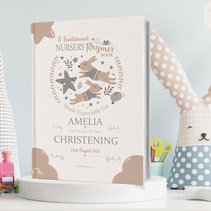 May include: A light pink book with a traditional nursery rhyme theme. The cover features a star, two bunnies, and the text "A Traditional Nursery Rhymes Book". The book is personalised with the name "Amelia" and the date "23rd August 2022".