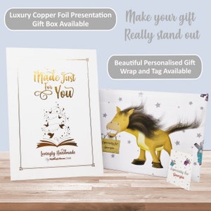 Op de afbeelding: Een witte cadeaudoos met een gouden folieontwerp. De doos heeft een gouden inscriptie met de tekst "Made Just For You" en "Lovingly Handmade by MyMagicName Books". De doos staat op een houten oppervlak. Een witte cadeauzak met een paardenillustratie en sterren is ook te zien. De tas heeft een label met de tekst "Especially for Georgia".