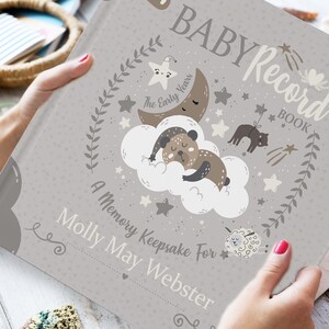 Puede incluir: Un libro de registro para beb&eacute;s de color gris con una linda ilustraci&oacute;n de un oso durmiendo en una nube con estrellas y una luna. El texto en la portada dice "Baby Record Book, The Early Years, A Memory Keepsake For Molly May Webster".