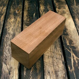 May include: A rectangular block of light brown wood, sitting on a dark brown wooden surface.