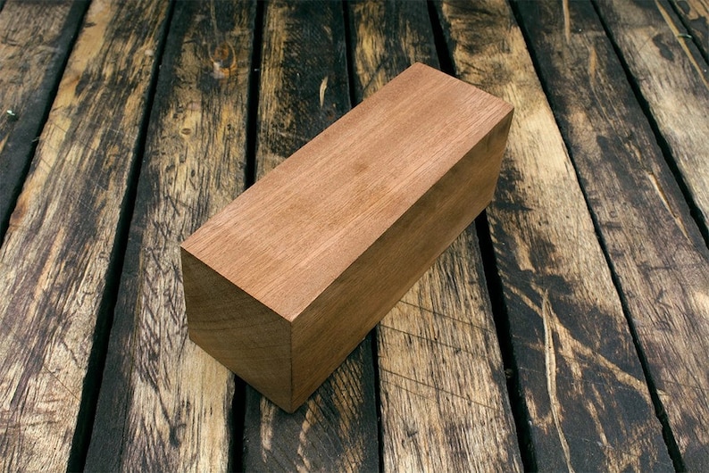 May include: A rectangular block of light brown wood, sitting on a dark brown wooden surface.