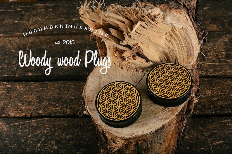May include: Two black wood plugs with a gold geometric design, displayed on a wood surface. The plugs are round with a flat top. The image includes the text "Woodwork in Ukraine est. 2015" and "Woody wood Plugs".
