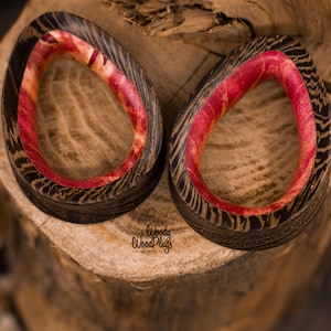 May include: Two wooden ear gauges with a red and black wood grain pattern. The gauges are shaped like a teardrop and have a smooth, polished finish.