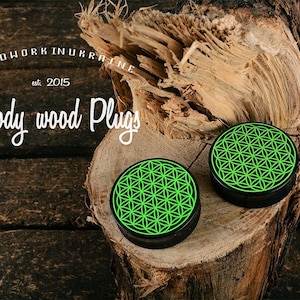 May include: Two black wood plugs with a neon green geometric design, displayed on a piece of wood. The plugs are round with a flat surface. The image also includes the text "Woodwork in Ukraine est. 2015" and "Woody wood Plugs".