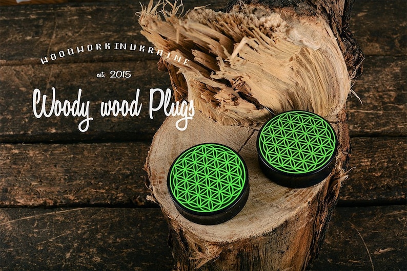 May include: Two black wood plugs with a neon green geometric design, displayed on a piece of wood. The plugs are round with a flat surface. The image also includes the text "Woodwork in Ukraine est. 2015" and "Woody wood Plugs".