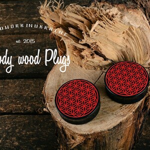 May include: Two wooden plugs with a black rim and a red geometric design, displayed on a piece of wood. The image includes the text "Woodwork in Ukraine est. 2015" and "Woody wood Plugs".