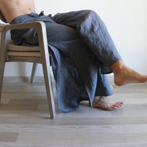 May include: A person sitting in a light wood chair with a white cushion. They are wearing loose-fitting, dark gray pants.