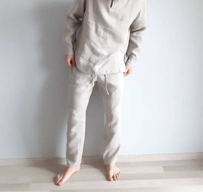 May include: A light beige linen pajama set with a long-sleeved top and pants. The top has a simple, round neckline and the pants have a drawstring waist.