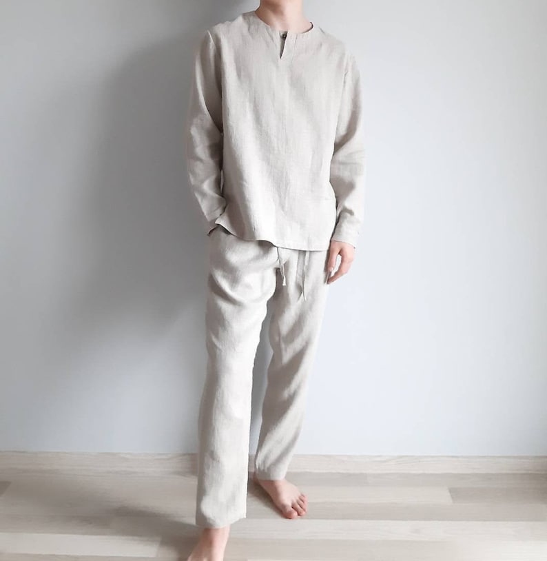 May include: A beige linen pajama set with a long-sleeved shirt and pants. The shirt has a V-neck and a button closure at the neckline. The pants have a drawstring waistband.