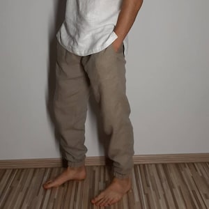 May include: A pair of light brown linen pants with a relaxed fit. The pants have a drawstring waist and a cuffed hem.