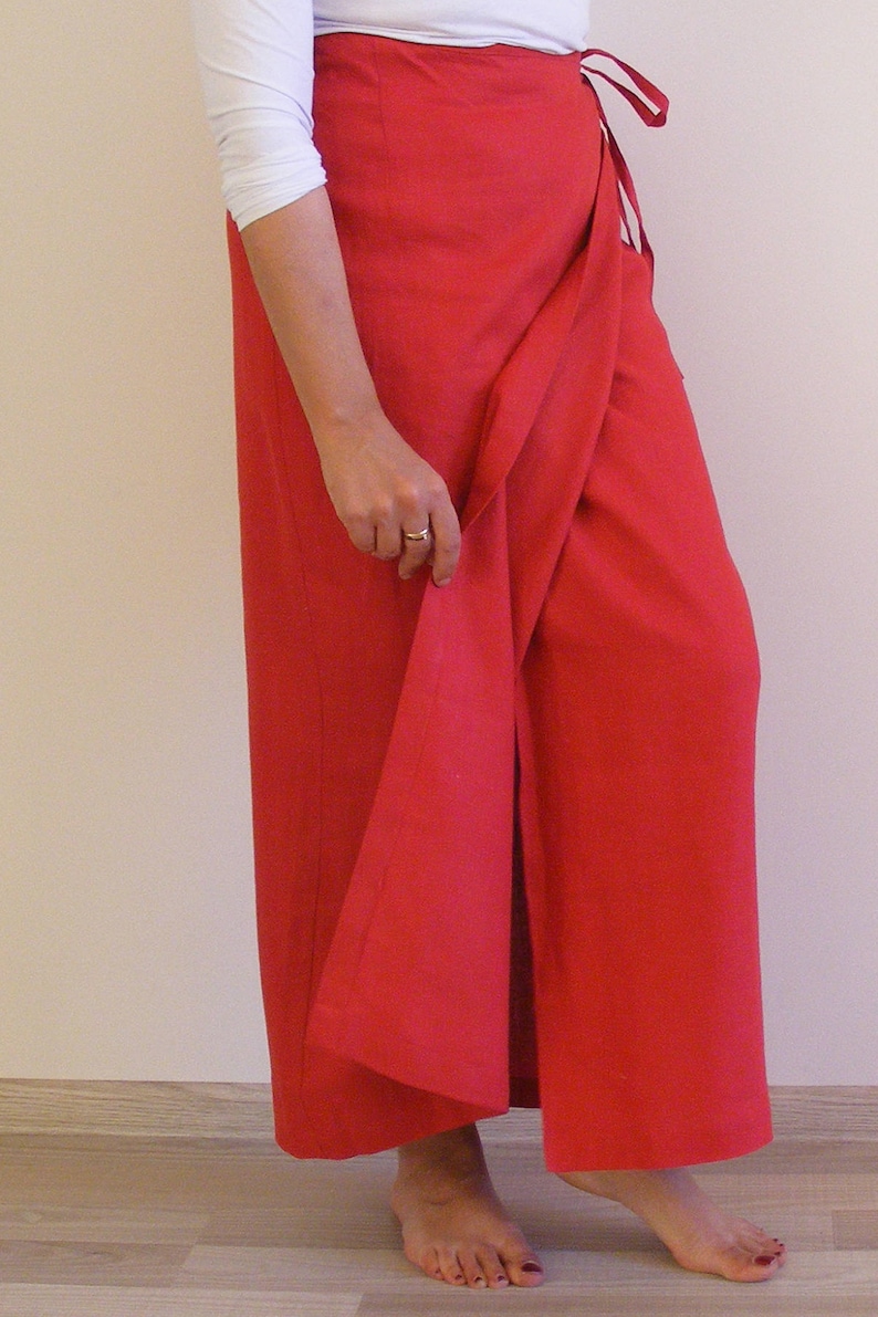 May include: A red wrap skirt with a long, flowing design. The skirt is tied at the waist with a thin fabric belt.