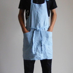 May include: A light blue linen apron with two large pockets and a tie waist.