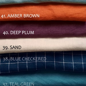 May include: A stack of fabric swatches in various colors, including mint green, amber brown, deep plum, sand, blue checkered, teal green, and light blue. Each swatch is labeled with a number and color name.
