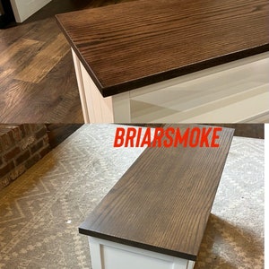 Puede incluir: Dos armarios de madera blanca con diferentes acabados de tinte para madera. El armario superior tiene un tinte marr&oacute;n oscuro etiquetado como "Kona" y el armario inferior tiene un tinte marr&oacute;n claro etiquetado como "Briarsmoke".