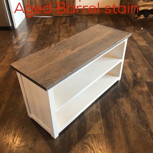 Puede incluir: Un banco de madera blanco con dos estantes y una tapa de roble con una mancha de barril envejecida. El banco est&aacute; sentado en un suelo de madera.