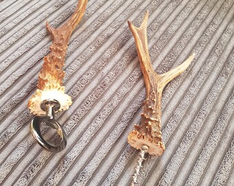 May include: Two antler bottle openers. One is a bottle opener with a ring, the other is a corkscrew. Both are made of antler and have a silver metal base.