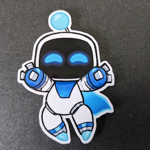 May include: A sticker featuring a cartoon robot character in white, black, and blue. The robot has a rounded head with a blue antenna and glowing blue eyes. It has a blue cape and is in a playful pose.