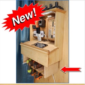 May include: A wall-mounted wooden organizer with a shelf, drawer, and storage compartments for power tools and accessories. It features a power strip, a charging station, and a built-in shelf for a tablet or phone. The organizer is made of light wood and has a natural finish.