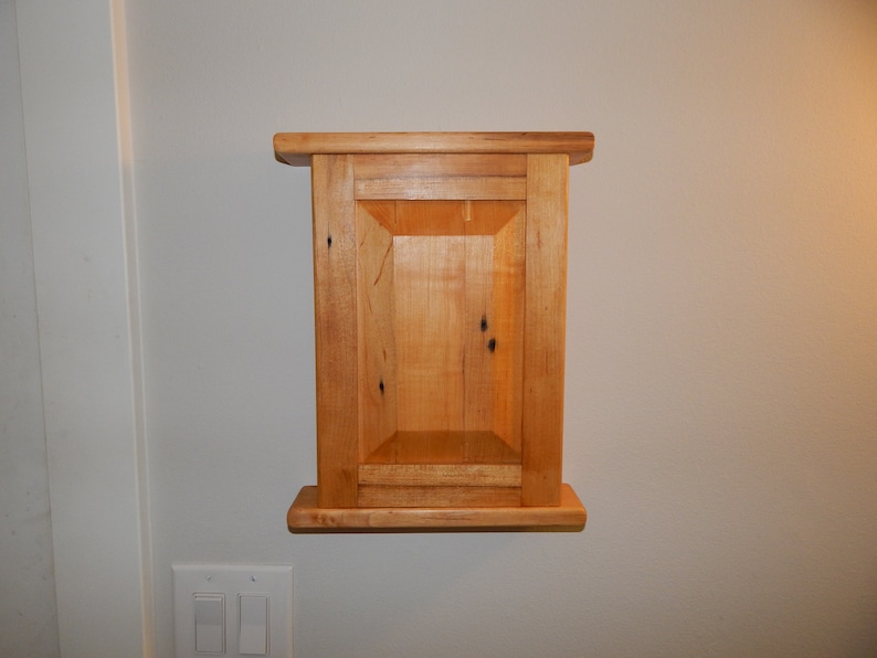 May include: A small wooden cabinet with a single door and a shelf. The cabinet is made of light wood with a natural finish.