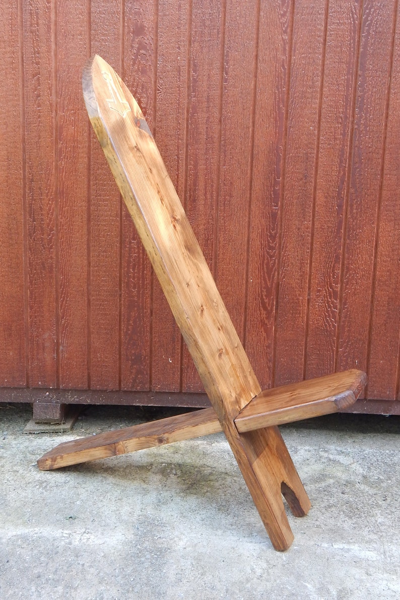 May include: A wooden folding chair with a simple design. The chair is made of natural wood and has a rustic look. The chair is in a folded position, with the back legs crossed over the front legs.