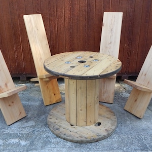 May include: A wooden table made from a cable spool with four simple wooden chairs. The table and chairs are all made from natural wood.