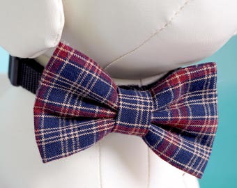May include: A plaid bow tie in shades of navy blue, burgundy, and cream. The bow tie is tied around the neck of a white stuffed animal.
