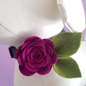 May include: A dark purple felt flower with green felt leaves attached to a black dog collar.