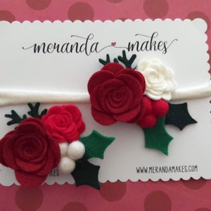 May include: Two felt Christmas flower headbands with red and white flowers, green holly leaves, and white berries. The headbands are white and are displayed on a white card with the text "meranda makes" and "www.merandamakes.com".